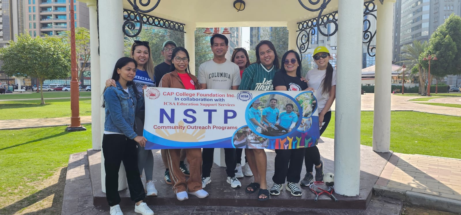 Community outreach volunteers holding an NSTP banner in a gazebo