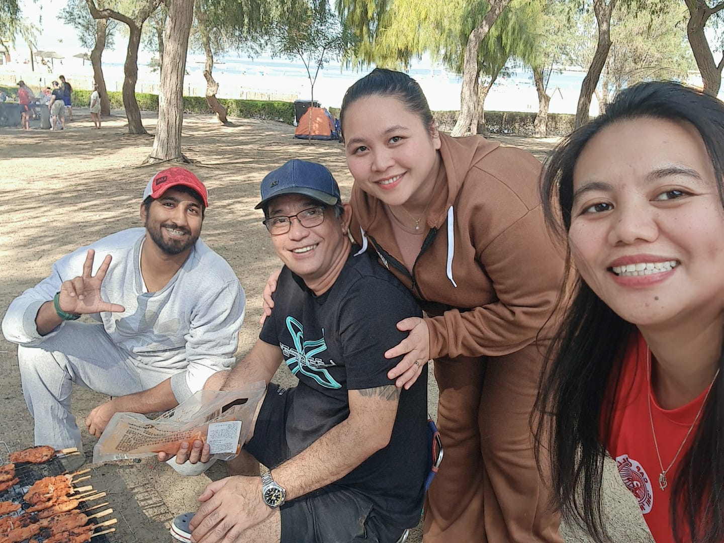 Friends smiling beside a barbecue grill at a beachside picnic